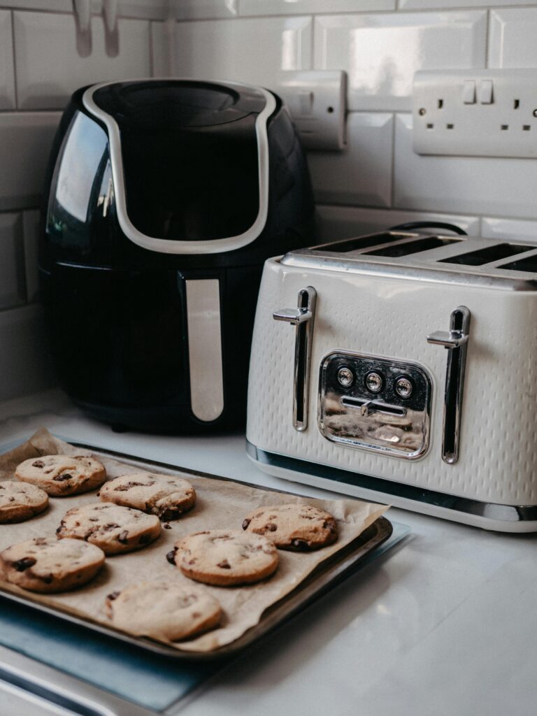 pexels-photo-29461935-29461935 Freshly baked cookies on tray beside air fryer and toaster.